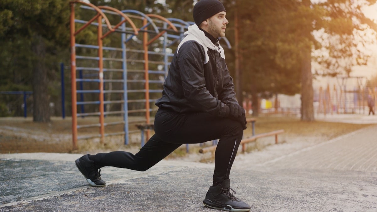 Young man runner doing stretching exercise preparing for morning workout and jogging in winter park